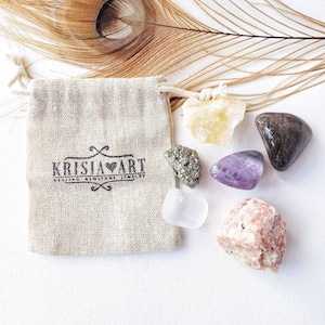 May include: A set of six tumbled crystals in a small burlap bag. The crystals are amethyst, clear quartz, citrine, pyrite, rose quartz, and black tourmaline. The bag has a logo that says "Krisia Art Healing Crystals Jewelry".