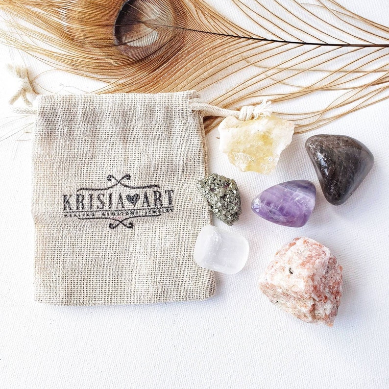 May include: A set of six tumbled crystals in a small burlap bag. The crystals are amethyst, clear quartz, citrine, pyrite, rose quartz, and black tourmaline. The bag has a logo that says "Krisia Art Healing Crystals Jewelry".