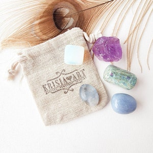 May include: A small pouch with the text "KRISLAKART" printed on it, containing five tumbled crystals: a clear crystal, a purple amethyst, a green and white crystal, a clear crystal, and a blue crystal.