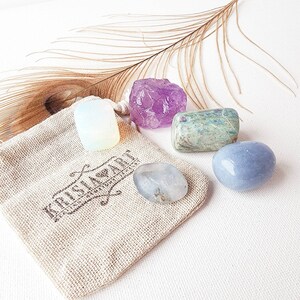 May include: A set of five tumbled crystals in a small burlap bag. The crystals are amethyst, clear quartz, moonstone, blue lace agate, and green aventurine.