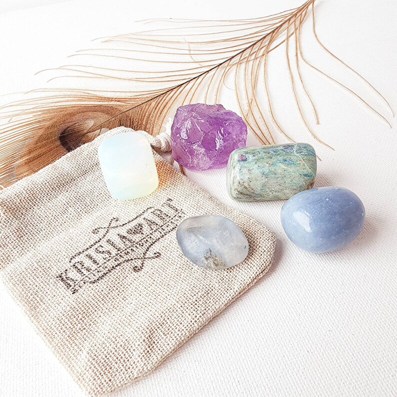 May include: A set of five tumbled crystals in a small burlap bag. The crystals are amethyst, clear quartz, moonstone, blue lace agate, and green aventurine.