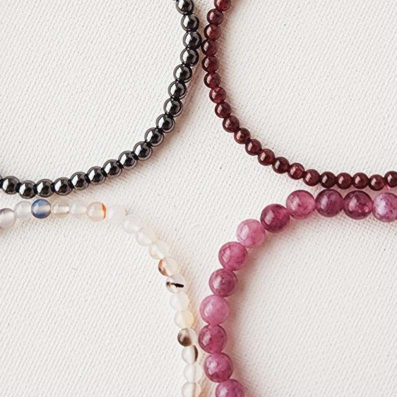 May include: Three beaded bracelets, one black, one burgundy, and one with white and pink beads.