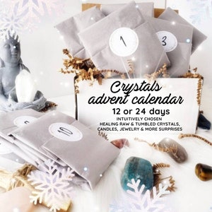 May include: A white box with a gray and white advent calendar filled with small gray envelopes. The box has the text "Crystals advent calendar 12 or 24 days INTUITIVELY CHOSEN HEALING RAW & TUMBLED CRYSTALS, CANDLES, JEWELRY & MORE SURPRISES".