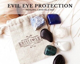 May include: A set of seven healing crystals in a small, white drawstring bag. The crystals are various colors, including black, white, blue, green, and gray. The bag has a brown logo that says "Kristal Art". The text "Evil Eye Protection Healing Crystals Set" is at the top of the image.