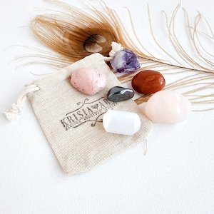 May include: A small pouch containing six tumbled crystals: amethyst, rose quartz, clear quartz, hematite, carnelian, and pink calcite. The pouch is made of natural fabric and has the text "Krisia Art" printed on it.