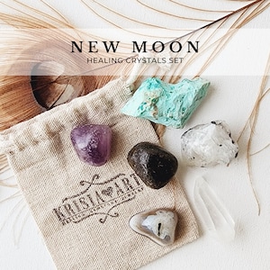 May include: A set of six crystals in a small, beige cloth bag. The crystals are amethyst, black obsidian, clear quartz, white quartz, and turquoise. The bag has the words "KRISTALLARO" printed on it. The text "NEW MOON HEALING CRYSTALS SET" is displayed above the bag.