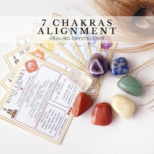 May include: Set of seven chakra healing crystals with corresponding cards. The crystals are arranged in a circle on a white background. The cards are spread out around the crystals. The cards have information about each chakra, including its color, crystals, essential oils, and affirmation.