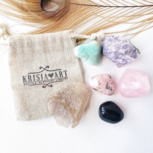 Puede incluir: Un conjunto de seis cristales pulidos en una peque&ntilde;a bolsa de arpillera. Los cristales son: amatista, cuarzo rosa, cuarzo transparente, aventurina verde, obsidiana negra y rodonita rosa. La bolsa tiene el texto "Krisia Art Healing Crystals Jewelry" impreso en ella.