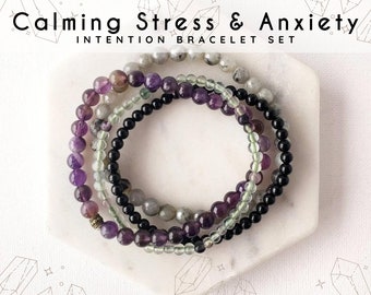 May include: An image of three beaded bracelets in shades of purple, green, black, and gray. The bracelets are displayed on a white, hexagonal surface. The text at the top reads "Calming Stress & Anxiety" and "Intention Bracelet Set".