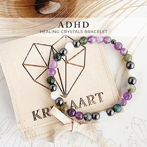 May include: A purple, green, and black crystal bracelet with a heart-shaped tag that says "ADHD Healing Crystals Bracelet" and "Krystalaart".