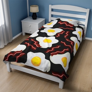 May include: A black twin bed with a white bed frame and a white and red patterned duvet cover featuring a repeating pattern of fried eggs and bacon.