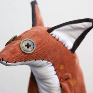 May include: A handmade plush fox toy with a brown corduroy body, white fabric ears with black trim, and a brown button eye.