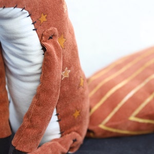 May include: A plush fox toy with a brown corduroy body and a white belly. The fox has a long, striped tail and gold stars on its body.