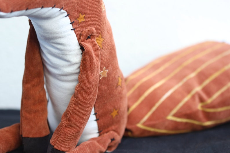 May include: A plush fox toy with a brown corduroy body and a white belly. The fox has a long, striped tail and gold stars on its body.