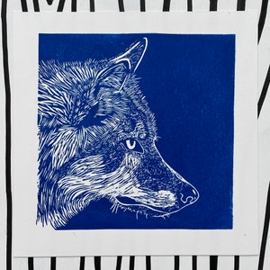 May include: A white line drawing of a wolf's head against a solid blue background.