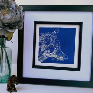 May include: A framed print of a white wolf's head against a blue background. The print is titled "The Wolf" and signed by the artist.