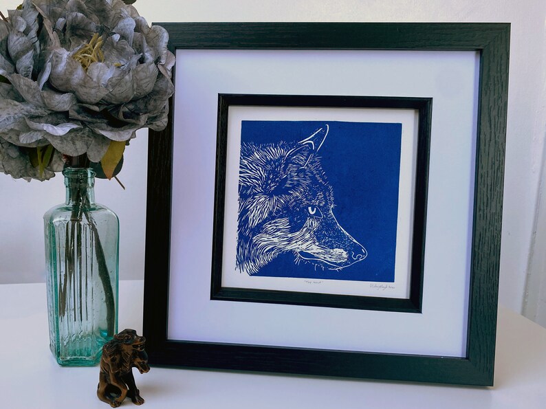 May include: A framed print of a white wolf's head against a blue background. The print is titled "The Wolf" and signed by the artist.
