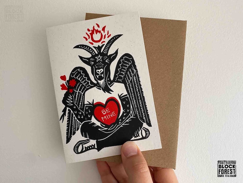 May include: A black and red Valentine's Day card featuring a black and white illustration of a devil holding a red heart with the text "Be Mine".