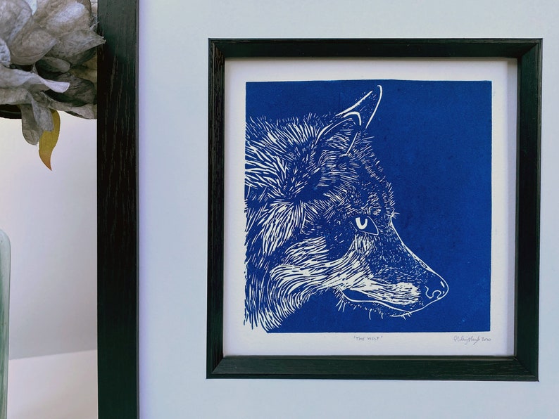 May include: A white wolf head print on a blue background. The print is framed in black and has the text "Wolf Head" and "R. Duffy-Singh 2020" at the bottom.
