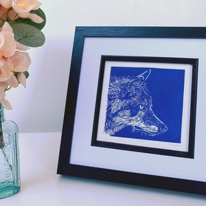 May include: A framed print of a white wolf's head on a blue background. The print is titled "The Wild".