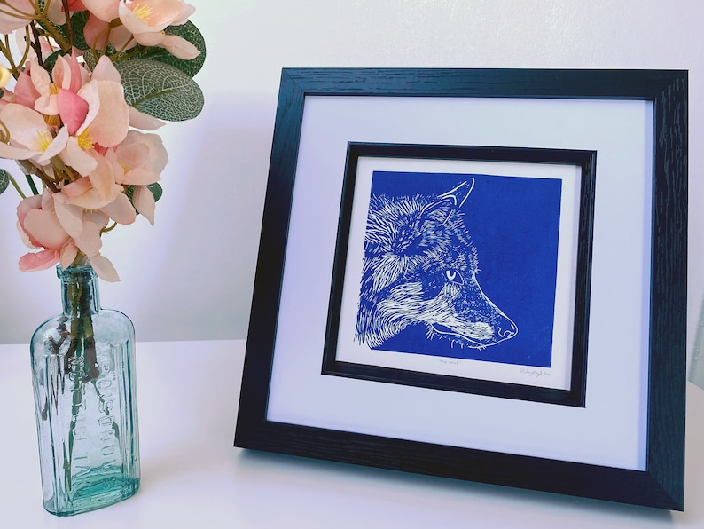 May include: A framed print of a white wolf's head on a blue background. The print is titled "The Wild".