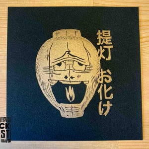 May include: A gold-colored illustration of a lantern with a smiling face and the Japanese text "提灯お化け" on a black background.