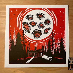 Puede incluir: Grabado en linóleo rojo y negro de una cabaña en el bosque con una luna llena con múltiples ojos en el cielo. La impresión se titula "Block Forest".