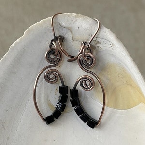 May include: Copper wire earrings with black square beads. The earrings are shaped like a teardrop with a spiral at the top.