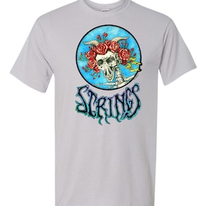 May include: A white t-shirt with a blue circle graphic featuring a skull with a crown of red roses and the word "STRINGS" in a colorful, gothic font.