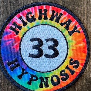 May include: A round, tie-dye patch with the words "Highway 33 Hypnosis" embroidered in black on a white background.