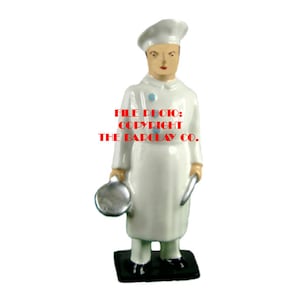 May include: White ceramic figurine of a chef wearing a white chef's hat and holding a silver pan and a knife. The figurine is standing on a black base. FILE PHOTO: COPYRIGHT THE BARCLAY CO.