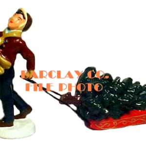 May include: A figurine of a person wearing a brown coat and a hat pulling a sled with a green Christmas tree on it.