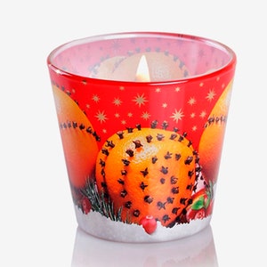 May include: A red glass candle holder with a Christmas-themed design featuring oranges studded with cloves, green pine branches, and red berries. The candle holder is filled with a white candle.