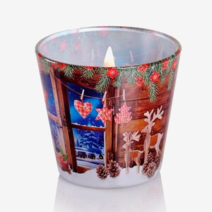 May include: A glass candle holder with a winter scene printed on it. The scene features a window with a snowy landscape outside, a wooden wall with a garland of pine branches and red berries, and a string of Christmas ornaments hanging from clothespins. The candle holder is lit with a white candle.