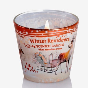 May include: A glass candle jar with a red and white winter scene featuring reindeer pulling a sleigh. The candle is lit and the jar has the text "Winter Reindeers Scented Candle with a mysterious aroma".