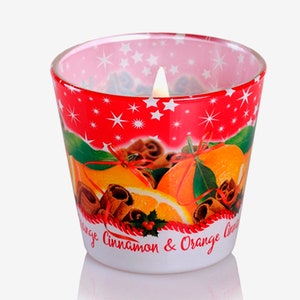 May include: A red glass candle jar with a white star pattern and a printed image of oranges, cinnamon sticks, and greenery. The text on the jar reads "Orange Cinnamon & Orange Lime".