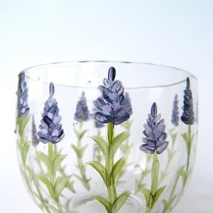 Hand-painted glass tumbler features a charming design of lavender flowers. The clear glass showcases delicate purple and green hues, creating a visually appealing and elegant piece. Perfect for adding a touch of nature-inspired beauty to any setting. The lavender floral design is hand-painted, adding a unique and artistic touch to the glass. This lovely tumbler is ideal for everyday use or special occasions.