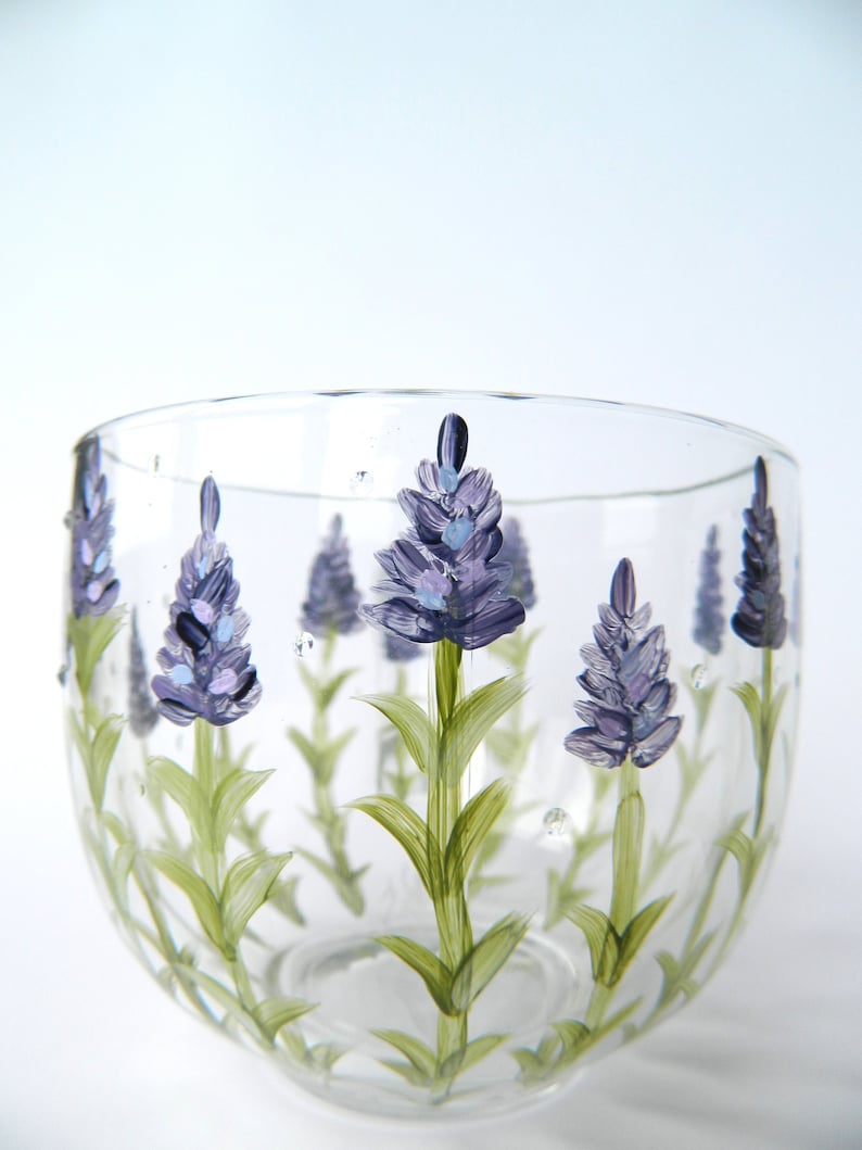 Hand-painted glass tumbler features a charming design of lavender flowers. The clear glass showcases delicate purple and green hues, creating a visually appealing and elegant piece. Perfect for adding a touch of nature-inspired beauty to any setting. The lavender floral design is hand-painted, adding a unique and artistic touch to the glass. This lovely tumbler is ideal for everyday use or special occasions.