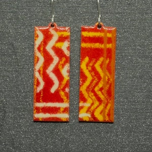 May include: A pair of red and yellow geometric patterned earrings. The earrings are rectangular and have a silver hook.