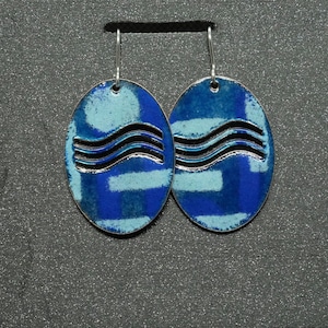 May include: A pair of blue and white oval earrings with a wavy line design. The earrings are made of metal and have a silver finish.