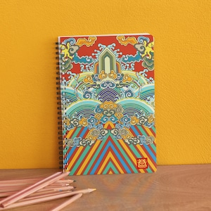 Peut inclure: Un carnet à spirales rouge, jaune, bleu et vert avec un motif d'inspiration asiatique coloré. La couverture présente un motif répétitif de nuages, de vagues et de formes géométriques. Le carnet a une reliure à spirales noire et un petit logo en bas à droite.