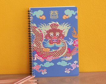 May include: A blue spiral notebook with a colorful dragon design and the text "SAIGON AUGUSTA" on the cover.