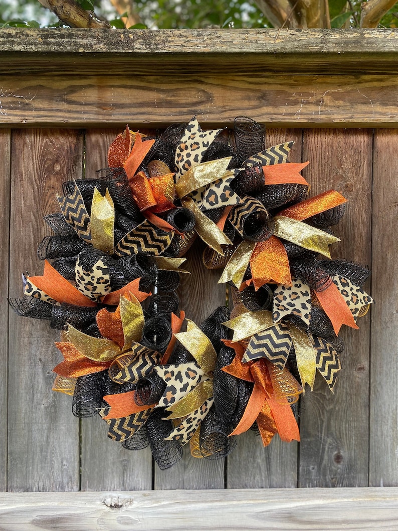 A black, gold, and orange wreath with leopard print, chevron, and glitter ribbon. The wreath is made of mesh and is decorated with various ribbons.