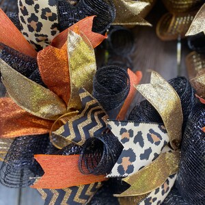 May include: A black, gold, and orange wreath with a leopard print, chevron, and mesh design.
