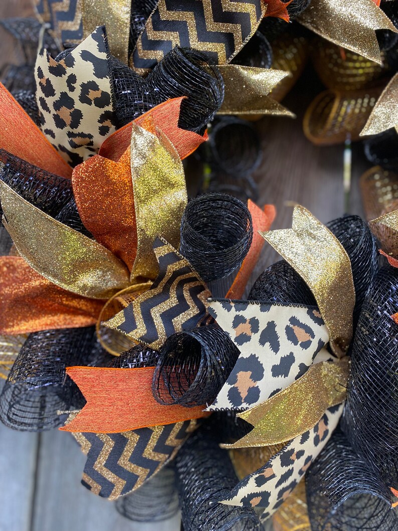 May include: A black, gold, and orange wreath with a leopard print, chevron, and mesh design.