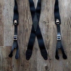 May include: Black suspenders with leather ends and a diamond-shaped leather back piece with the text "Genuine Leather" embossed on it.