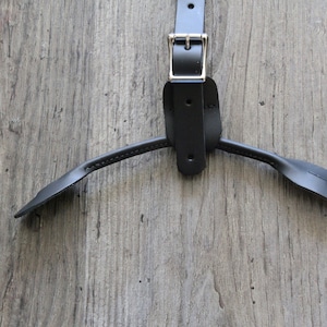 May include: Black leather suspenders with a silver buckle and adjustable straps. The straps are connected to a Y-shaped piece of leather.