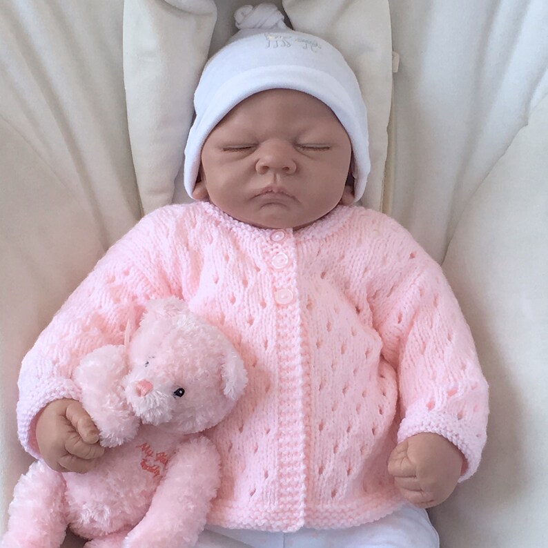 Mannequin wearing 0-3 month size pink eyelet lace baby cardigan with round neck, long sleeves and 3 button fastenings.