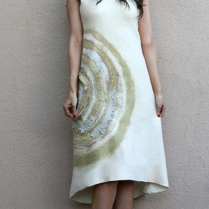 Puede incluir: Una mujer con un vestido blanco con un dise&ntilde;o circular verde y marr&oacute;n. Lleva gafas de sol y tiene el pelo recogido hacia atr&aacute;s. Est&aacute; de pie frente a una pared de color marr&oacute;n claro.