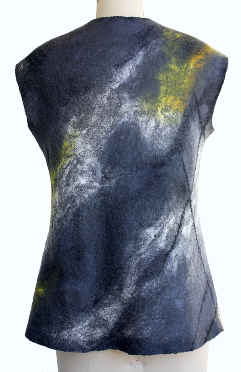 Puede incluir: Un chaleco sin mangas hecho de lana felpuda con una base de color azul oscuro y patrones abstractos blancos y amarillos.